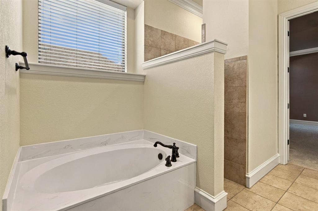 7004 Cherrybark Lane, North Richland Hills, TX 76182 Built-in soaking tub with a white finish and dark bronze fixtures, framed by a window with blinds