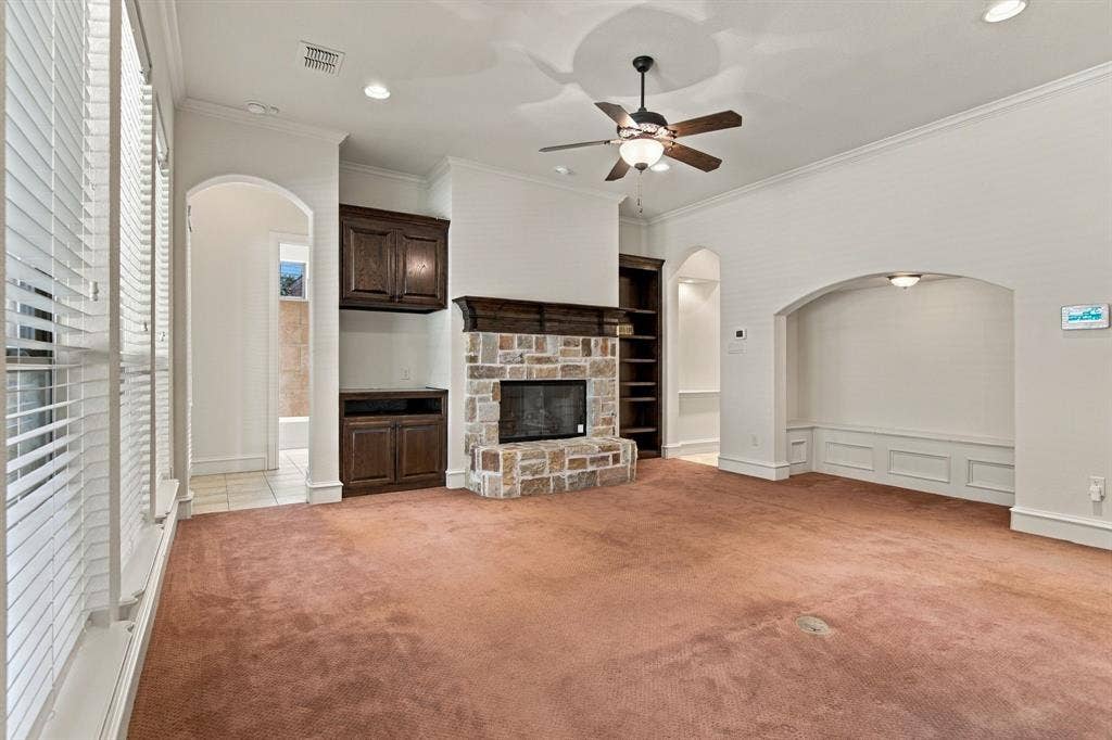 7004 Cherrybark Lane, North Richland Hills, TX 76182 Arched entryways, built-in shelving, stone-faced fireplace with wood mantel, built-in dark wood cabinetry, and a ceiling fan with integrated lighting