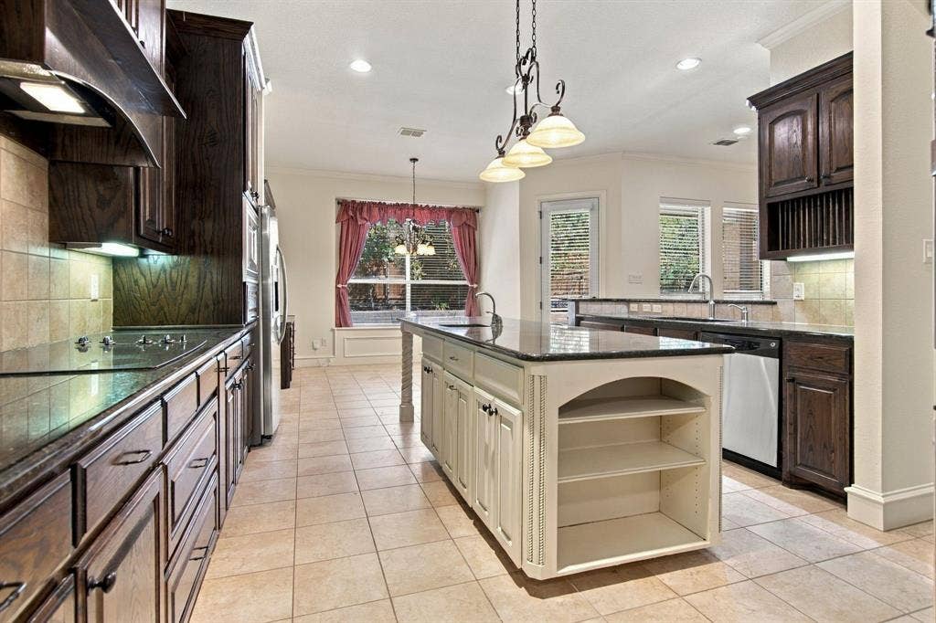 7004 Cherrybark Lane, North Richland Hills, TX 76182 Spacious kitchen featuring an island with built-in shelving, dark wood cabinetry, stainless steel appliances, and tile flooring