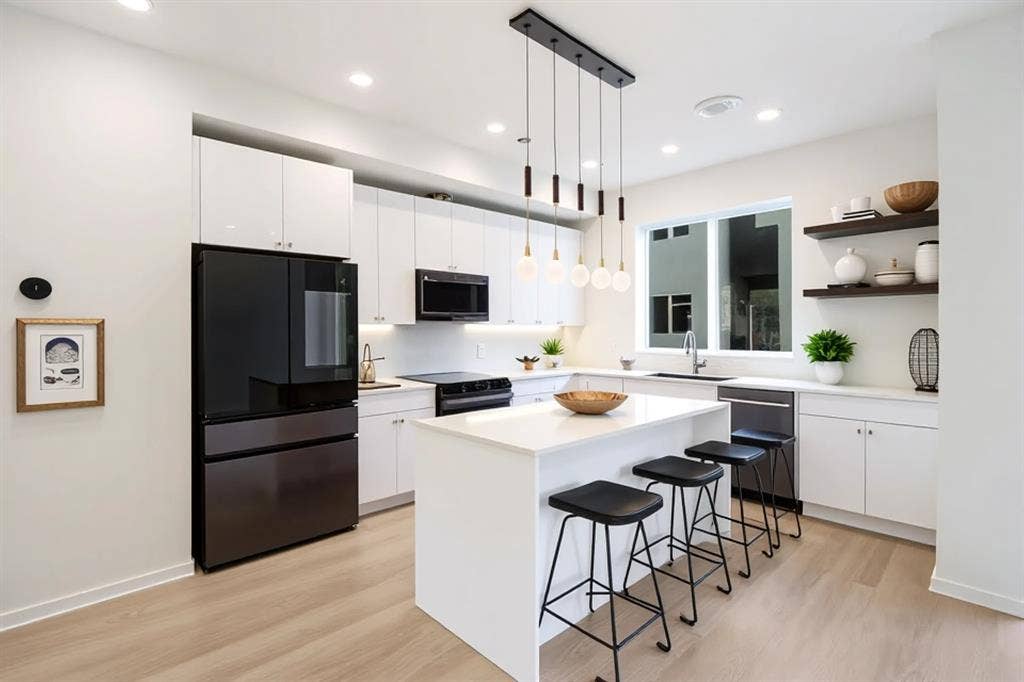 4811 Denton Drive, #201, Dallas, TX 75219 Gourmet kitchen featuring a central island, pendant lighting, stainless steel appliances, white cabinetry, and wood-finish flooring