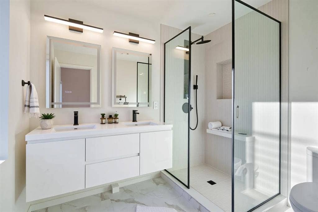 4811 Denton Drive, #201, Dallas, TX 75219 Dual floating vanity with integrated sinks and matte black fixtures, framed mirrors with overhead lighting, and a glass-enclosed walk-in shower with a built-in bench