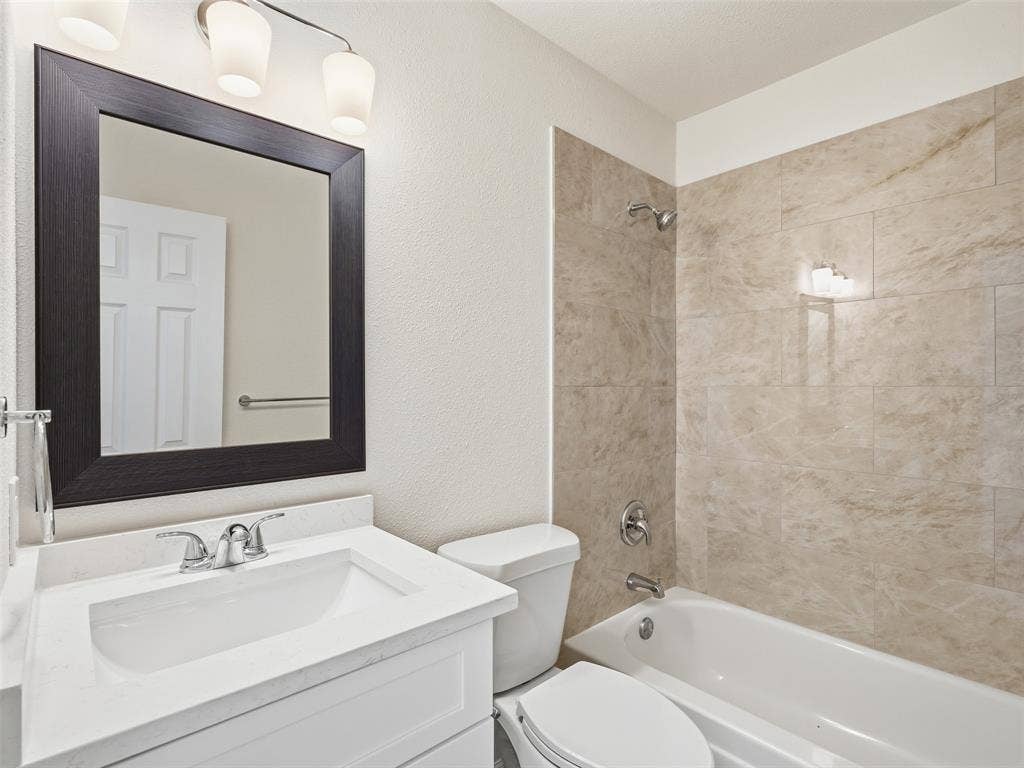 Bathroom with a vanity, integrated sink, framed mirror, and a bathtub with tiled surround