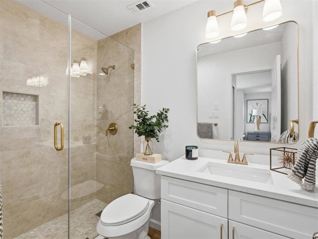 Frameless glass shower enclosure with brass hardware, a built-in shower niche, and mosaic tile flooring