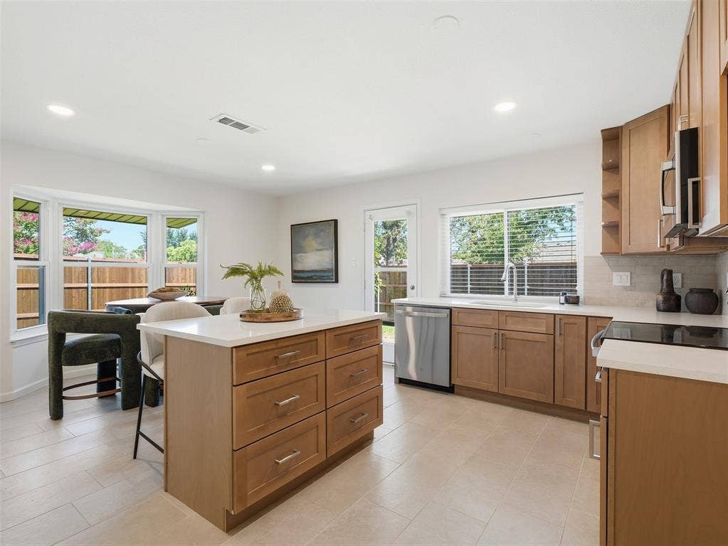 Kitchen featuring a center island with storage, light wood cabinetry, white countertops, stainless steel appliances, and tile flooring