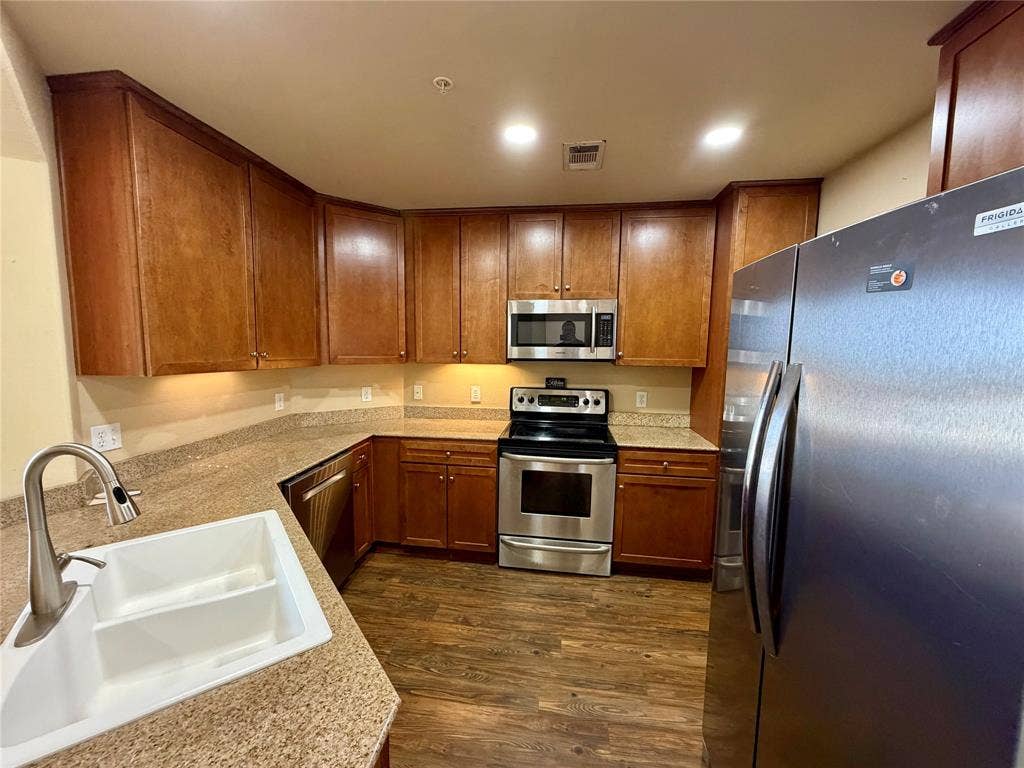 330 Las Colinas Boulevard E, #1006, Irving, TX 75039 Kitchen featuring wood-finish cabinetry, stone-look countertops, a stainless steel appliance package, and wood-finish flooring