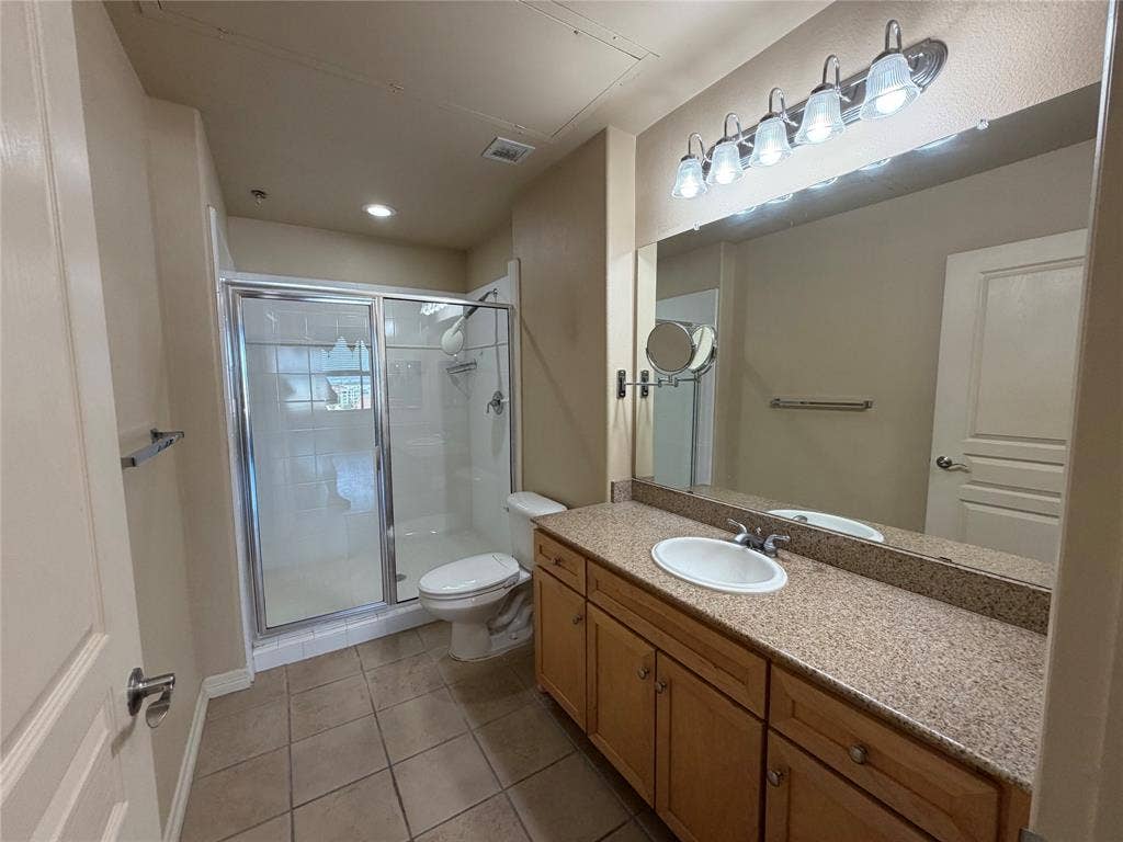 330 Las Colinas Boulevard E, #1006, Irving, TX 75039 Tiled flooring, wood-finish vanity with ample storage, integrated sink, large vanity mirror, and shower enclosure with sliding glass door