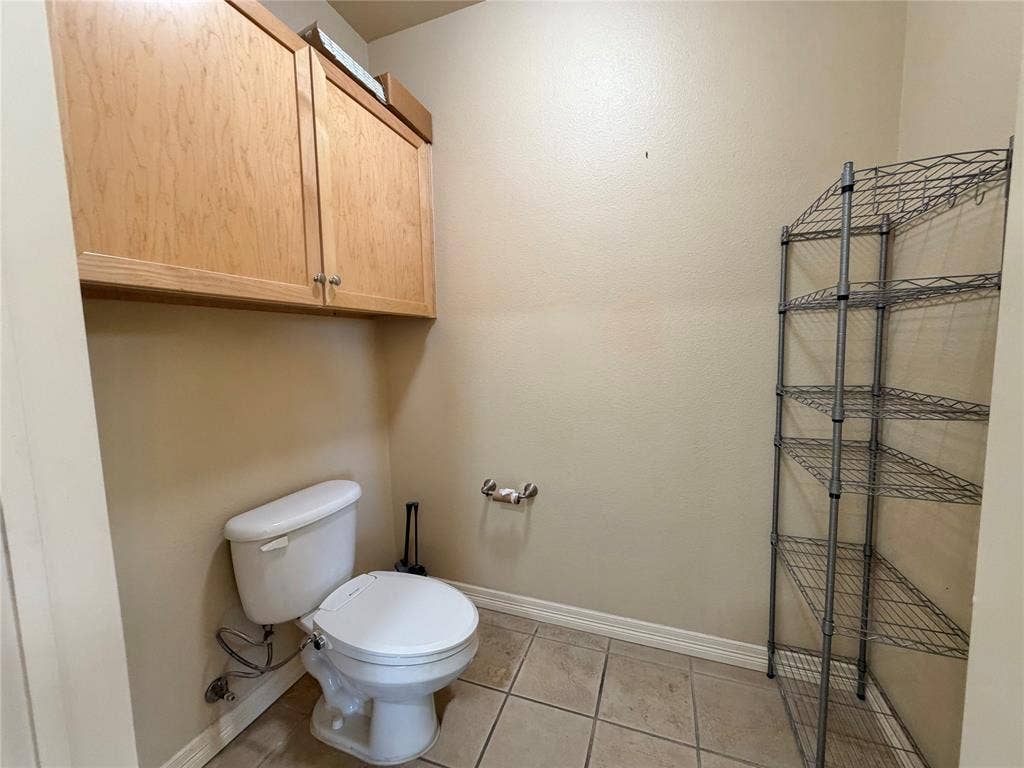 330 Las Colinas Boulevard E, #1006, Irving, TX 75039 Overhead cabinetry with wood-finish doors and metal pulls, alongside a white toilet, and tiled flooring