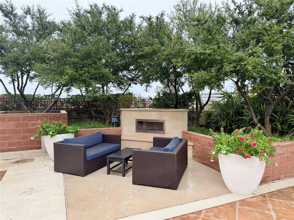 330 Las Colinas Boulevard E, #1006, Irving, TX 75039 Tiled patio area with a built-in outdoor fireplace, surrounded by raised brick planters and mature trees