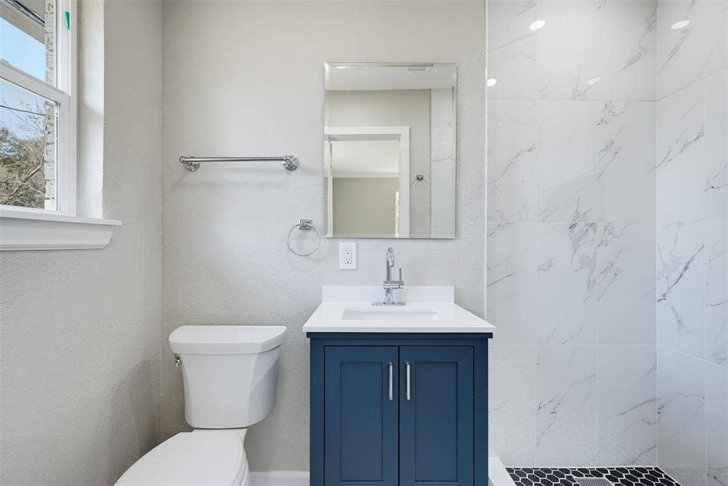 1312 E Mitchell Street, Arlington, TX 76010 Bathroom featuring a blue vanity with a white countertop, a white toilet, white wall tiling, and black hexagonal floor tiling in the shower