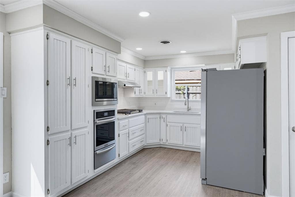 1312 E Mitchell Street, Arlington, TX 76010 White cabinetry with beadboard accents, stainless steel appliances, recessed lighting, wood-finish flooring, and a countertop-mounted sink