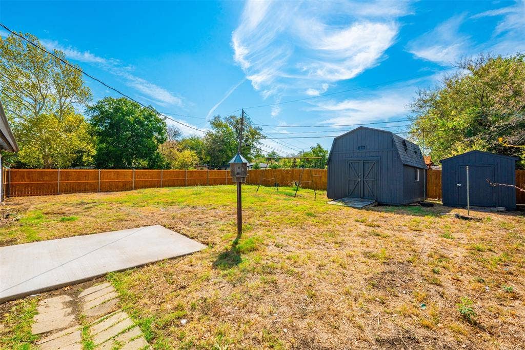 1312 E Mitchell Street, Arlington, TX 76010 Expansive backyard featuring a new wood privacy fence, concrete patio area, and two detached storage sheds