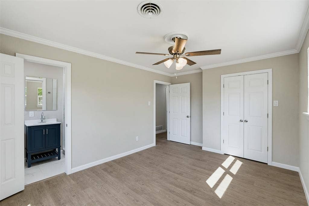 1312 E Mitchell Street, Arlington, TX 76010 Wood-finish flooring, ceiling fan with integrated lighting, white crown molding, white painted trim, and a built-in closet with bi-fold doors