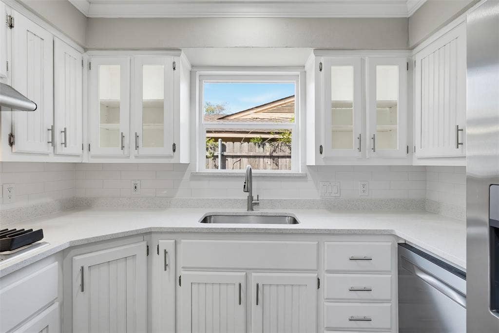 1312 E Mitchell Street, Arlington, TX 76010 White cabinetry with glass-front uppers, stainless steel sink with a gooseneck faucet, light-toned countertops, and subway tile backsplash