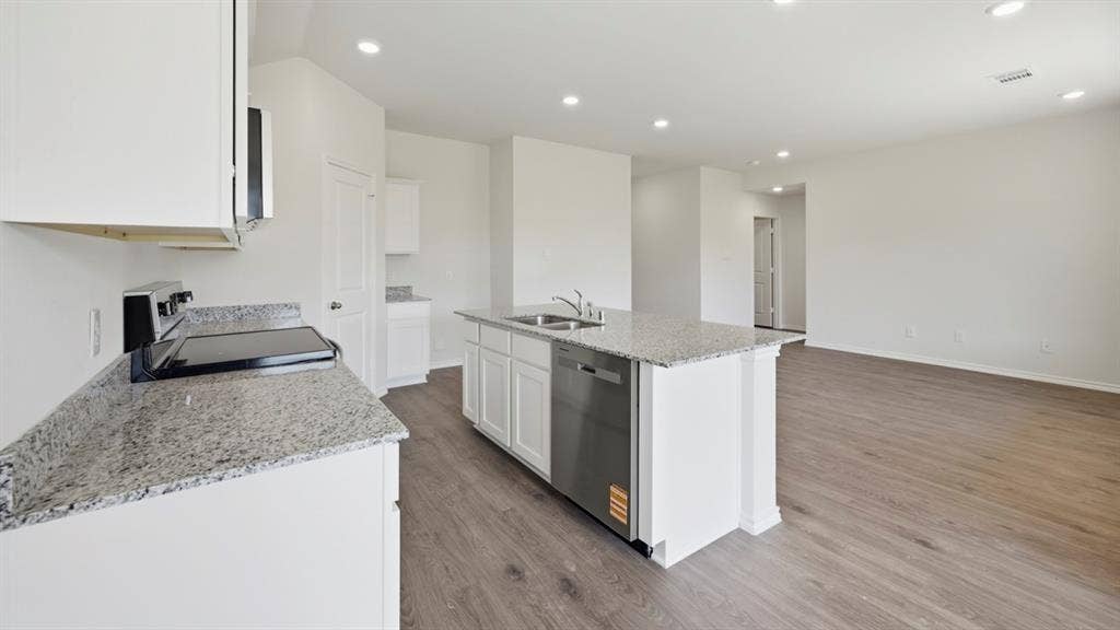 1916 Freeman Street, Tyler, TX 75704 Open-concept kitchen featuring an island with a stainless steel sink and dishwasher, white cabinetry, speckled countertops, and wood-finish flooring