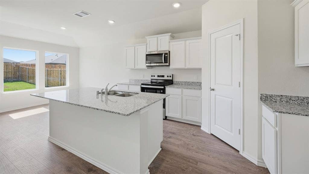 1916 Freeman Street, Tyler, TX 75704 Open-concept kitchen featuring an island with a double basin sink, white cabinetry, speckled countertops, and wood-finish flooring