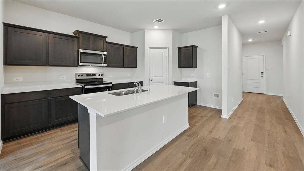 1928 Freeman Street, Tyler, TX 75704 Modern kitchen featuring dark wood cabinetry, stainless steel appliances, a center island with sink, white countertops, and wood-finish flooring