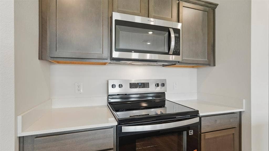 1924 Freeman Street, Tyler, TX 75704 Modern kitchen featuring grey shaker-style cabinetry, white countertops, stainless steel microwave, and a black and stainless steel electric range