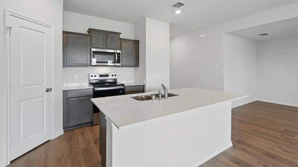 1924 Freeman Street, Tyler, TX 75704 Kitchen featuring dark wood cabinetry, stainless steel microwave, black electric range, and a white countertop island with an integrated sink