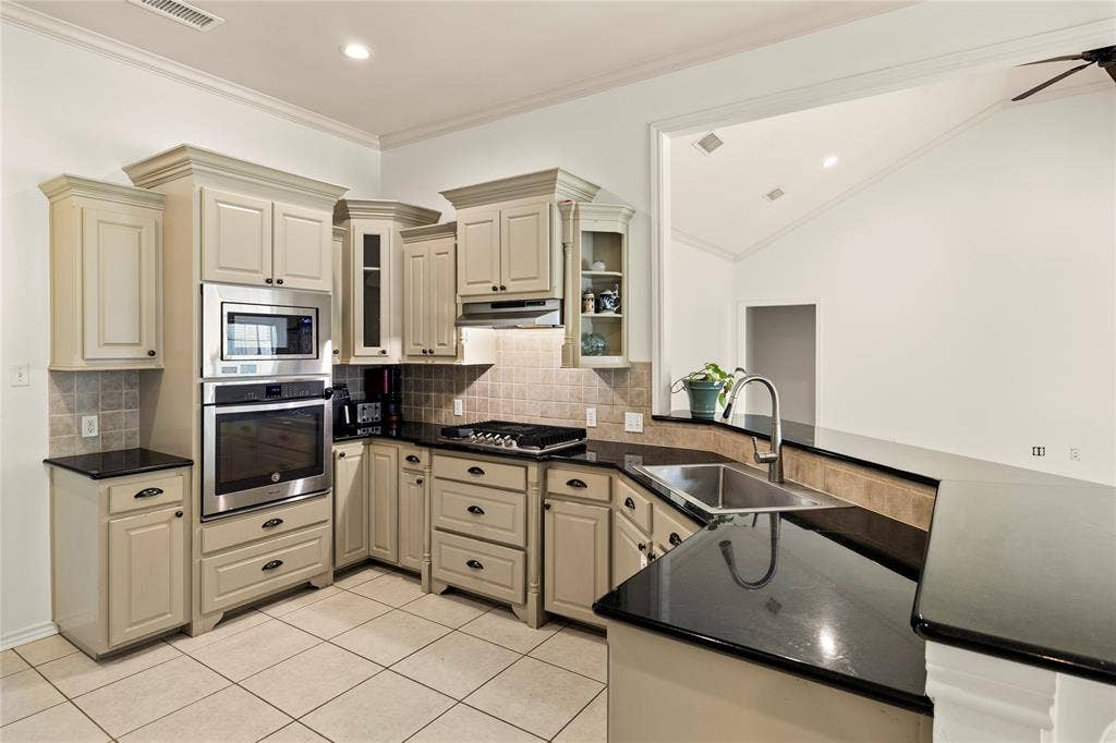 618 Huntwick Lane, Tyler, TX 75703 Kitchen featuring stainless steel built-in appliances, dark countertops, a tile backsplash, and light cabinetry with crown molding