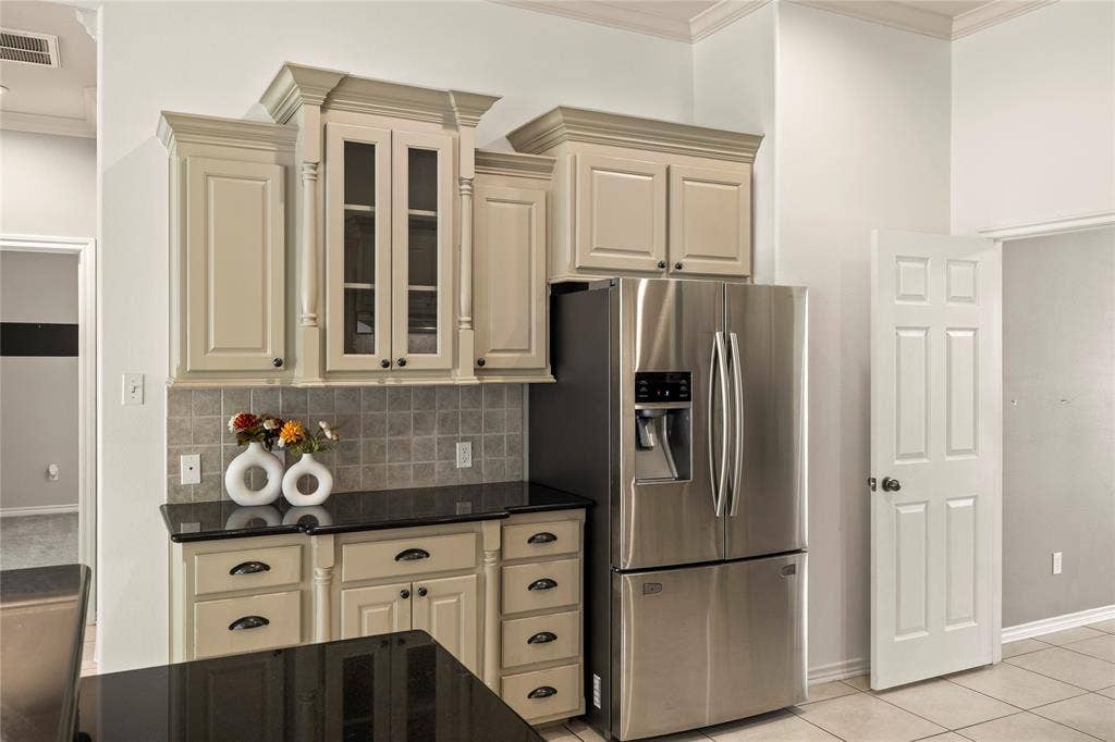 618 Huntwick Lane, Tyler, TX 75703 Built-in stainless steel refrigerator, light-toned cabinetry with crown molding, glass-front upper cabinets, dark countertops, and tiled backsplash