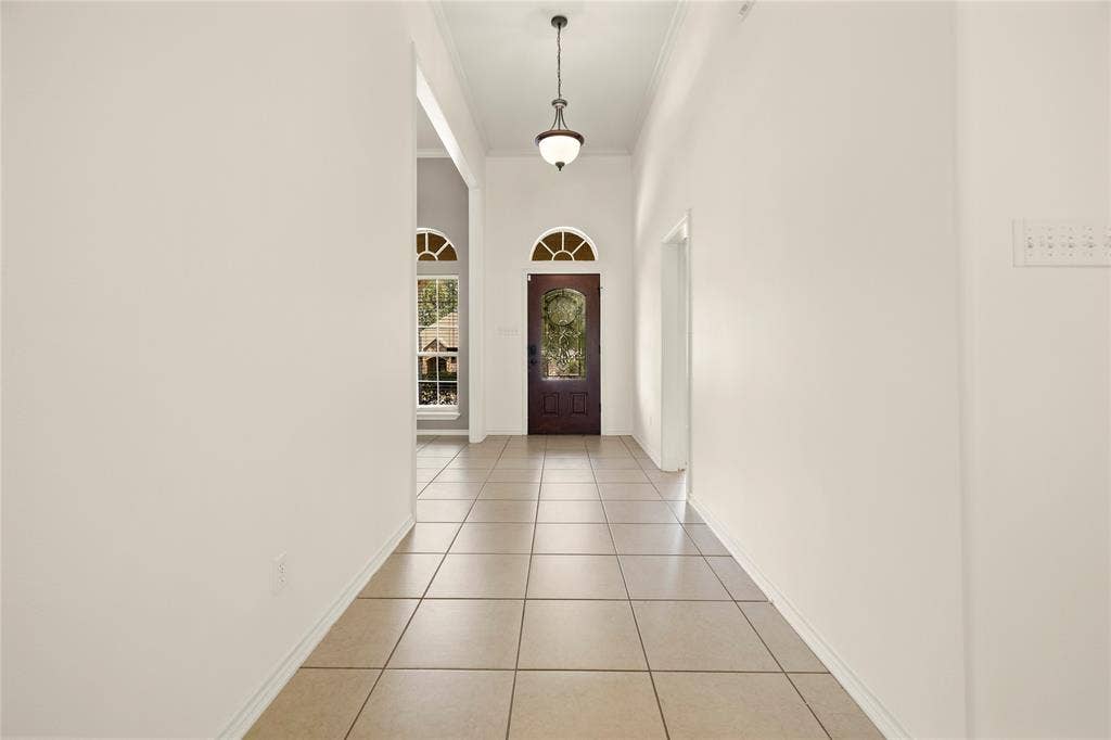 618 Huntwick Lane, Tyler, TX 75703 Tiled flooring extending through a hallway with arched doorways, a dark wood-finish door with an arched transom window, and a decorative pendant light fixture