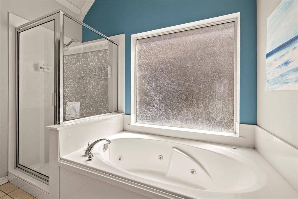 618 Huntwick Lane, Tyler, TX 75703 Built-in jetted tub with polished chrome fixtures, adjacent shower enclosure with glass door, and a frosted privacy window