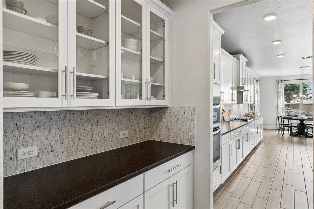 3707 Roth Drive, McKinney, TX 75071 Thoughtfully designed butler's pantry that features glass-front cabinetry, extensive lower storage, elegant mosaic backsplash, and generous counter space for entertaining and everyday organization.