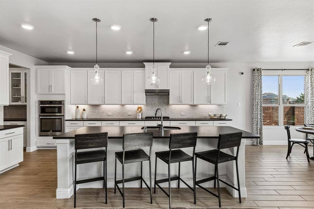 3707 Roth Drive, McKinney, TX 75071 Gourmet-inspired kitchen features an abundance of crisp white cabinetry, generous dark countertops, subway-style mosaic backsplash, stainless appliances, oversized island, and ample workspace.