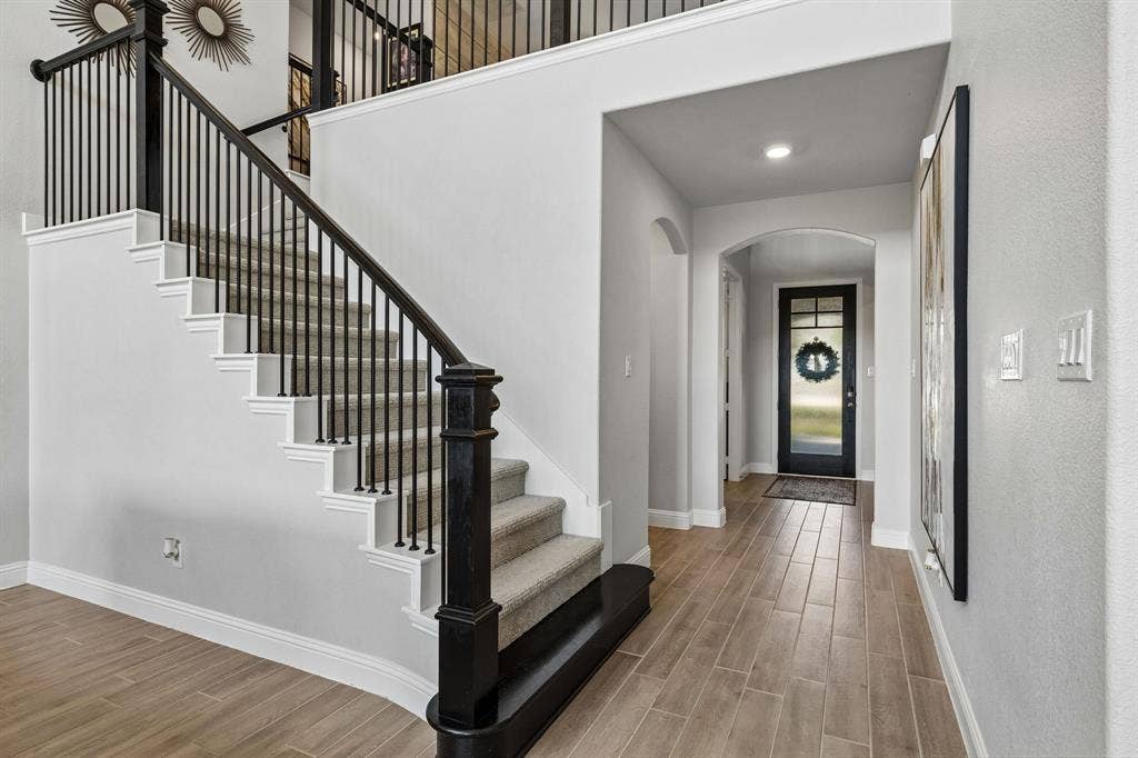 3707 Roth Drive, McKinney, TX 75071 Dramatic entry welcomes guests with soaring ceilings, elegant arched passageways, wood-look tile flooring, and a striking staircase accented by black wrought-iron balustrades