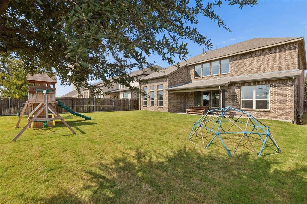 3707 Roth Drive, McKinney, TX 75071 Impressive rear elevation showcases the home's handsome brick architecture, expansive windows, covered patio, and beautifully proportioned two-story design. The broad backyard provides exceptional space for recreation, entertaining, gardening, or creating a personalized outdoor retreat.