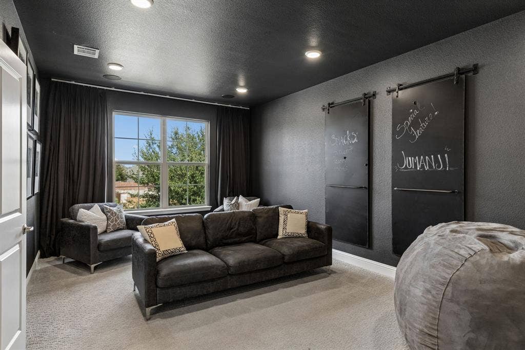 3707 Roth Drive, McKinney, TX 75071 Sophisticated media room creates an inviting destination for movie nights and entertaining, featuring rich charcoal walls and ceiling, recessed lighting, comfortable seating area, and custom chalkboard-style barn doors that add a distinctive designer touch.