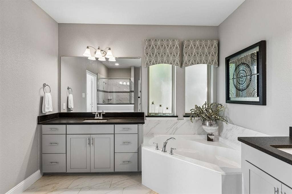 3707 Roth Drive, McKinney, TX 75071 This elegant primary bath showcases an expansive vanity with generous storage, sophisticated dark countertops, oversized mirror, refined fixtures, and a calming neutral palette.