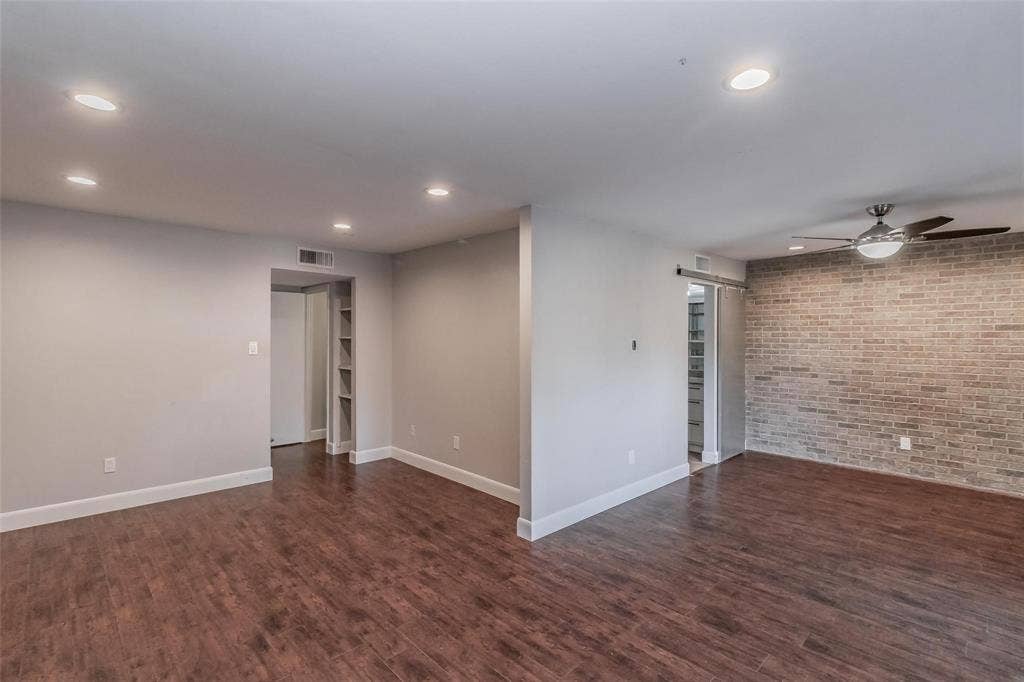 4930 Thunder Road, Dallas, TX 75244 Wood-finish flooring throughout, recessed ceiling lighting, a ceiling fan with integrated lighting, a brick-finish accent wall, and a barn door leading to an interior space with built-in shelving