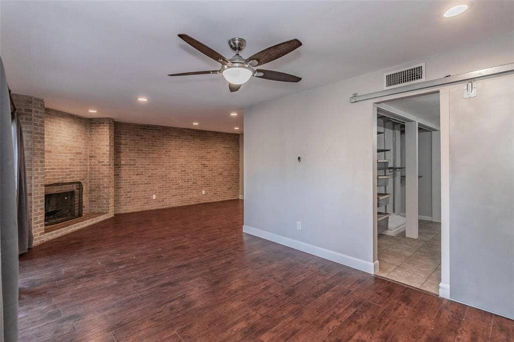 4930 Thunder Road, Dallas, TX 75244 Wood-finish flooring, exposed brick wall with fireplace, recessed lighting, ceiling fan, and barn door entry to an additional space
