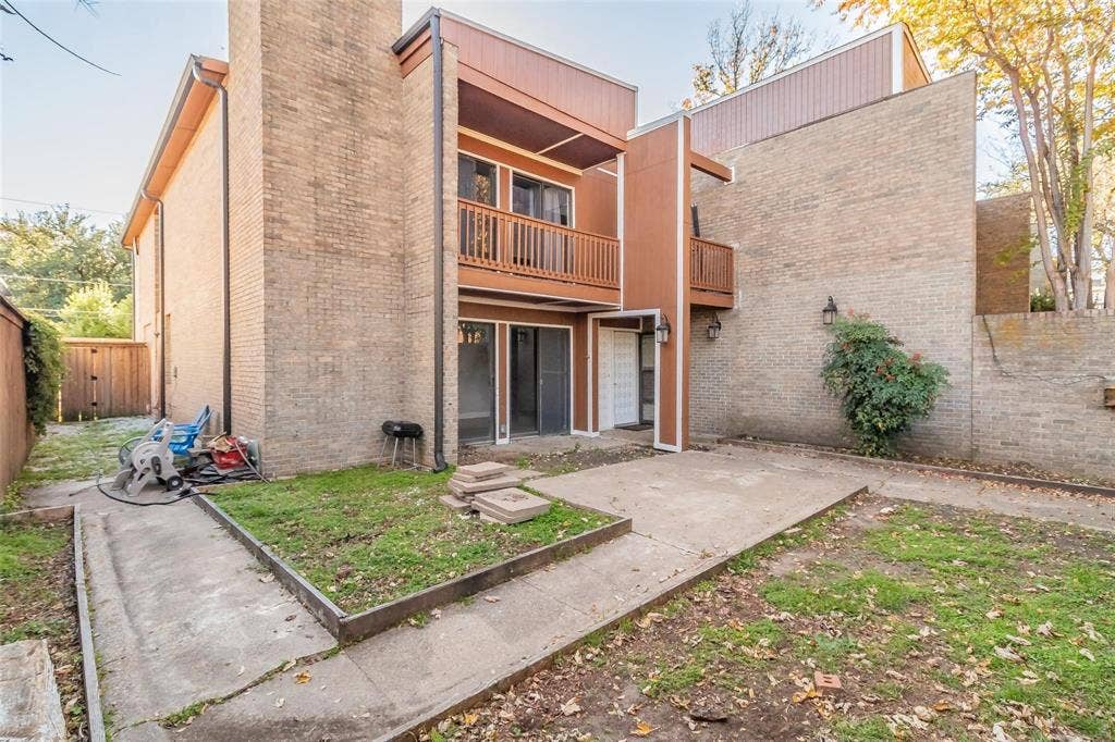 4930 Thunder Road, Dallas, TX 75244 Brick exterior with a second-story wood-finish balcony, ground-level patio door, and concrete patio area