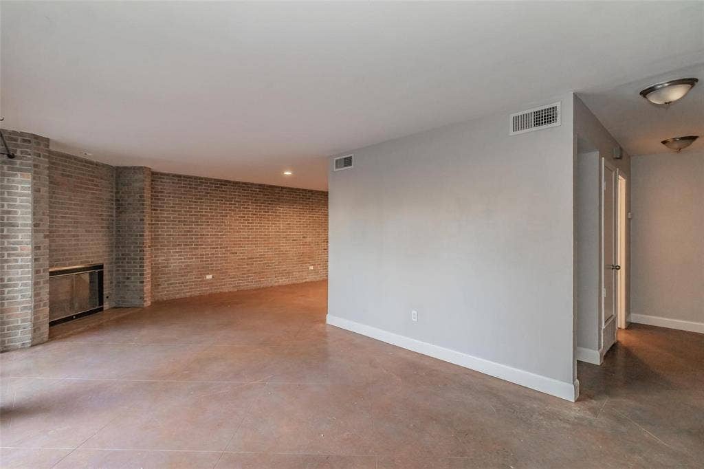 4930 Thunder Road, Dallas, TX 75244 Exposed brick wall, recessed lighting, fireplace with a glass enclosure, light gray painted walls, and concrete-finish flooring