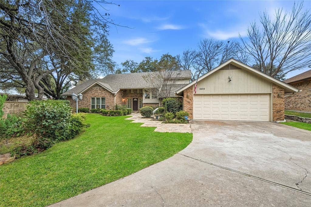 4424 Westridge Avenue, Fort Worth, TX 76116 Brick Colonial home showcasing a circular driveway, two-car garage with white paneled doors, manicured lawn with mature trees, and a welcoming entry featuring a covered portico with stone detailing