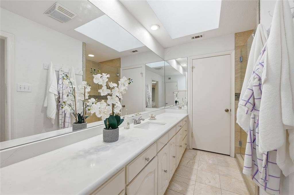 4424 Westridge Avenue, Fort Worth, TX 76116 Dual vanity with integrated sinks, expansive wall-mounted mirror, light-toned tile flooring, and a skylight