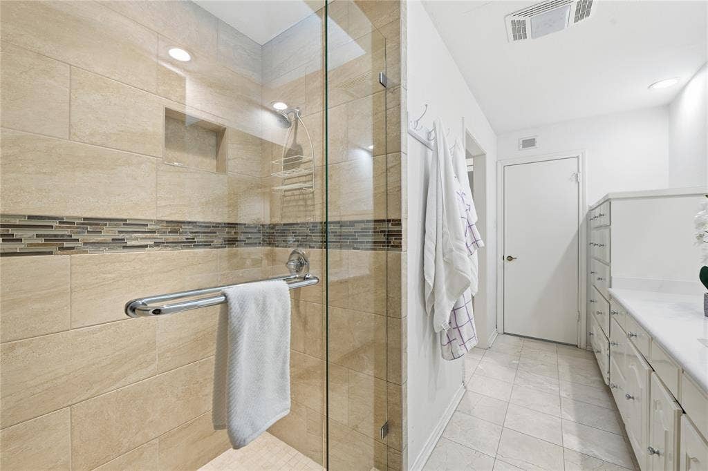 4424 Westridge Avenue, Fort Worth, TX 76116 Spa-inspired primary bathroom featuring a frameless glass-enclosed shower with dual showerheads, linear accent tile detailing, and a spacious soaking tub