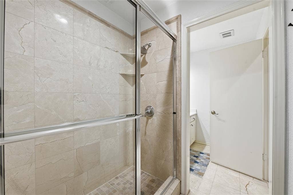 4424 Westridge Avenue, Fort Worth, TX 76116 Shower enclosure with sliding glass doors, tile surround, recessed shelving, and a tiled shower pan