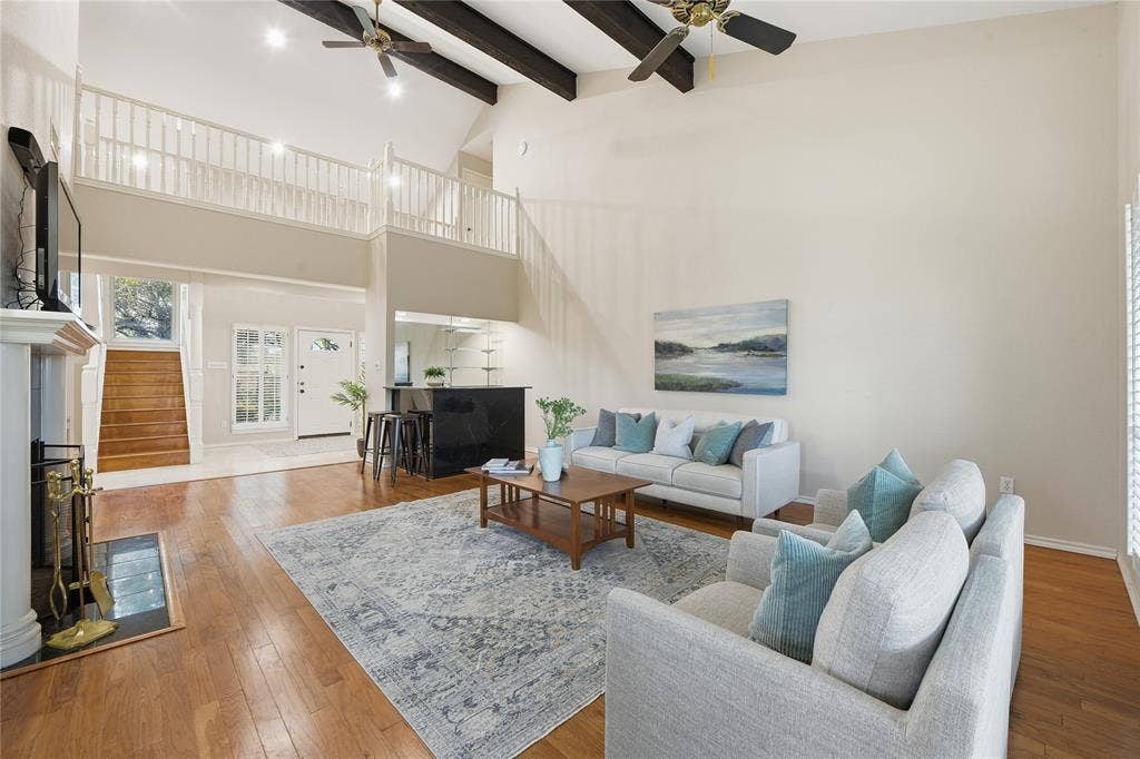 4424 Westridge Avenue, Fort Worth, TX 76116 Vaulted ceiling with exposed wood beams and ceiling fans, wood-finish flooring, white fireplace with mantle, built-in wet bar, and upper-level balcony