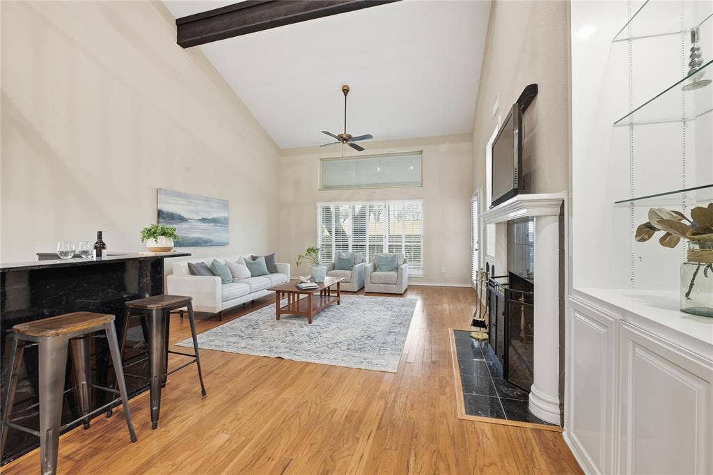 4424 Westridge Avenue, Fort Worth, TX 76116 Vaulted ceiling with exposed beam, wood-finish flooring, fireplace with white mantel, built-in cabinetry with glass shelving, and a wet bar with a dark countertop