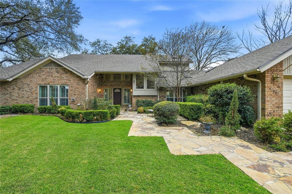 4424 Westridge Avenue, Fort Worth, TX 76116 Brick exterior with a gabled roofline, stone pathway, manicured front lawn, and mature landscaping