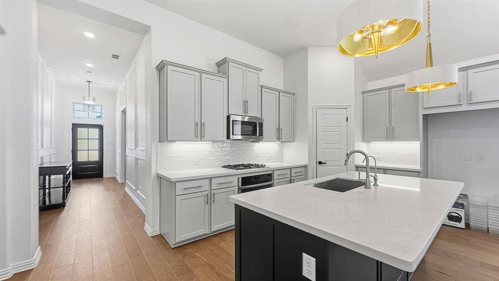 3129 Grayslick Avenue, Celina, TX 75009 Kitchen featuring light gray cabinetry, stainless steel microwave, white subway tile backsplash, and a large island with an undermount sink
