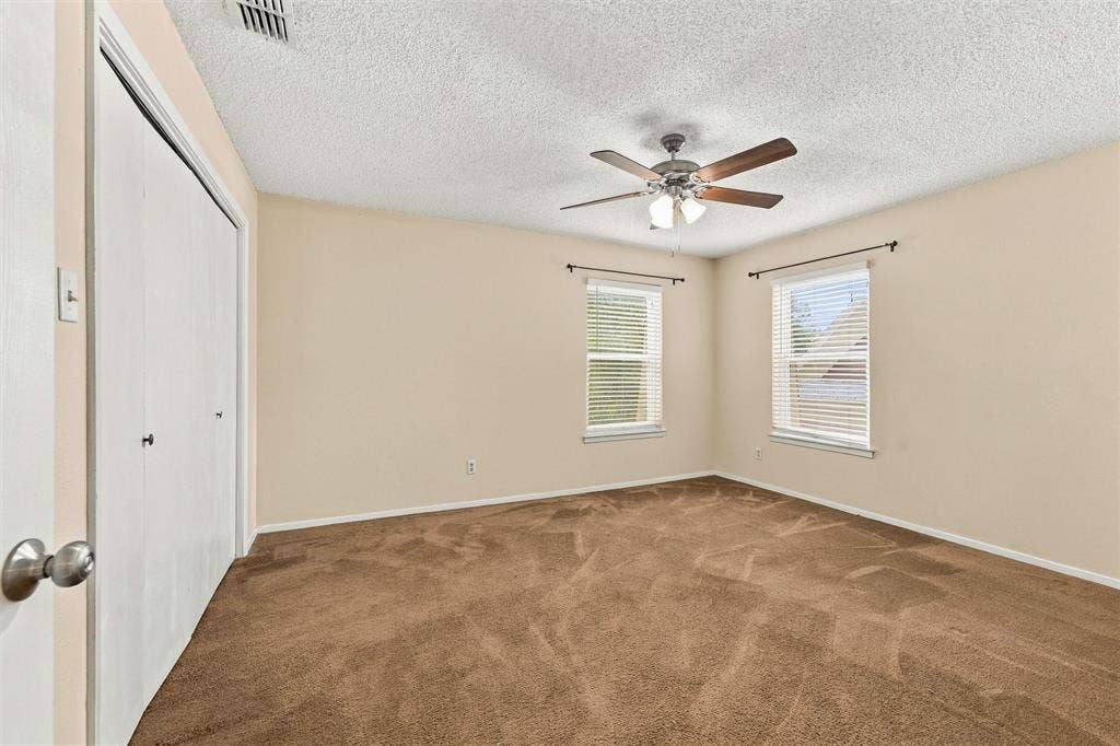 410 W Franklin Street, #5, Waxahachie, TX 75165 Brown carpeted flooring, two windows with blinds, a ceiling fan with light fixture, and a white bi-fold closet door