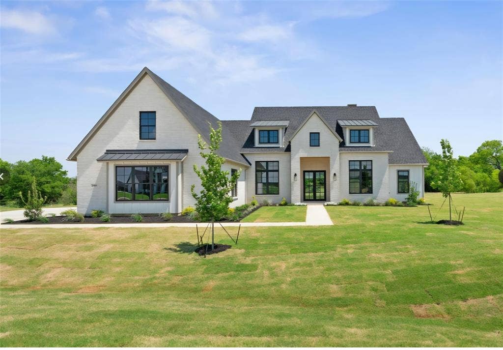 2608 Southbay, Northlake, TX 76226 White brick exterior with a dark shingle roof, black-framed windows, and an arched entry