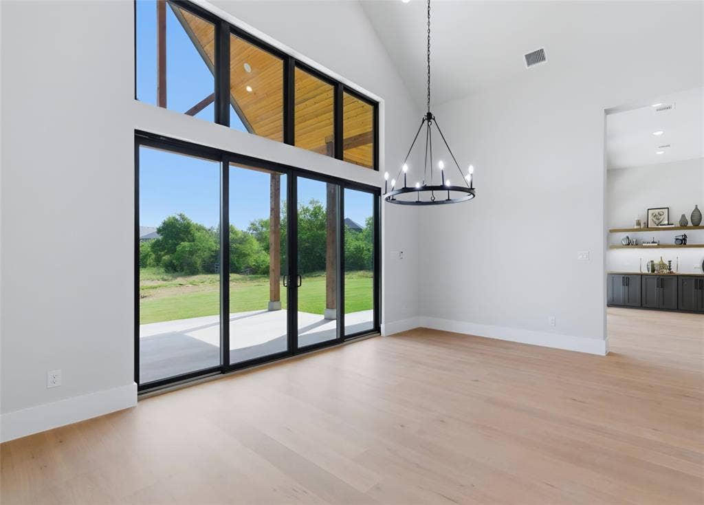 2608 Southbay, Northlake, TX 76226 Vaulted ceiling with wood-finish accents, large sliding glass doors, light wood-finish flooring, contemporary chandelier, and built-in shelving with lower cabinetry