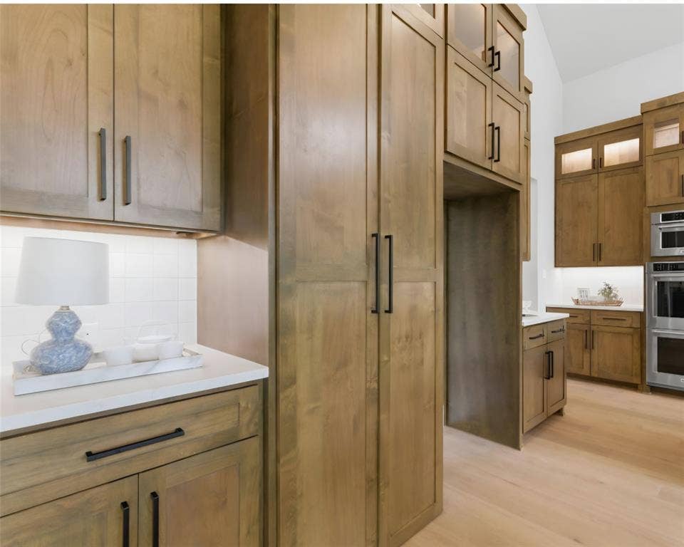 2608 Southbay, Northlake, TX 76226 Wood-finish cabinetry with black hardware, light wood-finish flooring, white countertops, white subway tile backsplash, and built-in stainless steel appliances