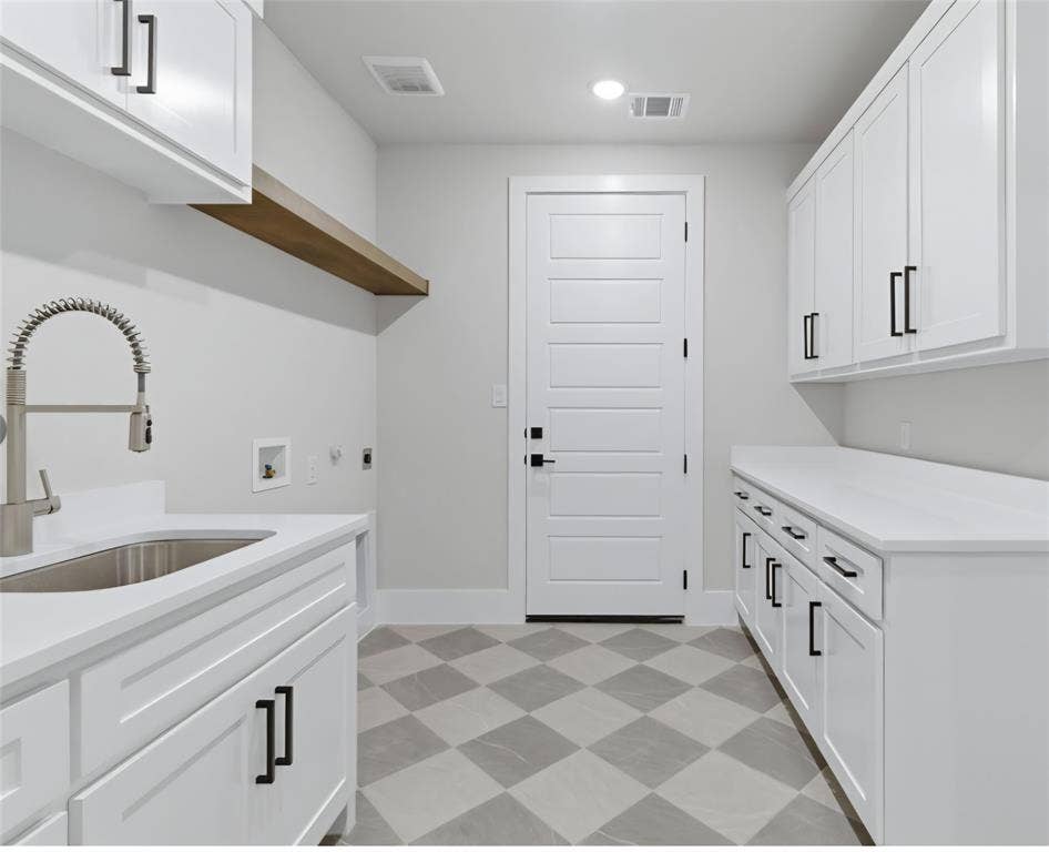 2608 Southbay, Northlake, TX 76226 White cabinetry with black hardware, stone-finish countertops, stainless steel sink with pull-down faucet, wood-finish floating shelf, and patterned floor tiling