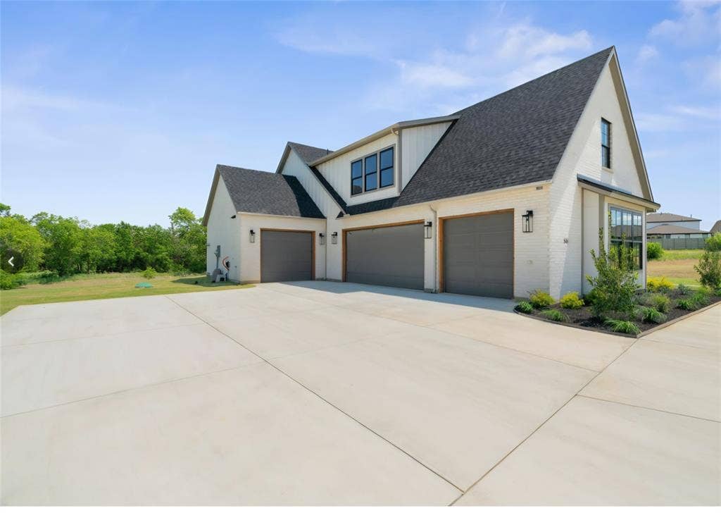 2608 Southbay, Northlake, TX 76226 Three-car garage with gray doors, white brick exterior, dark roof, accent windows, and landscaped beds